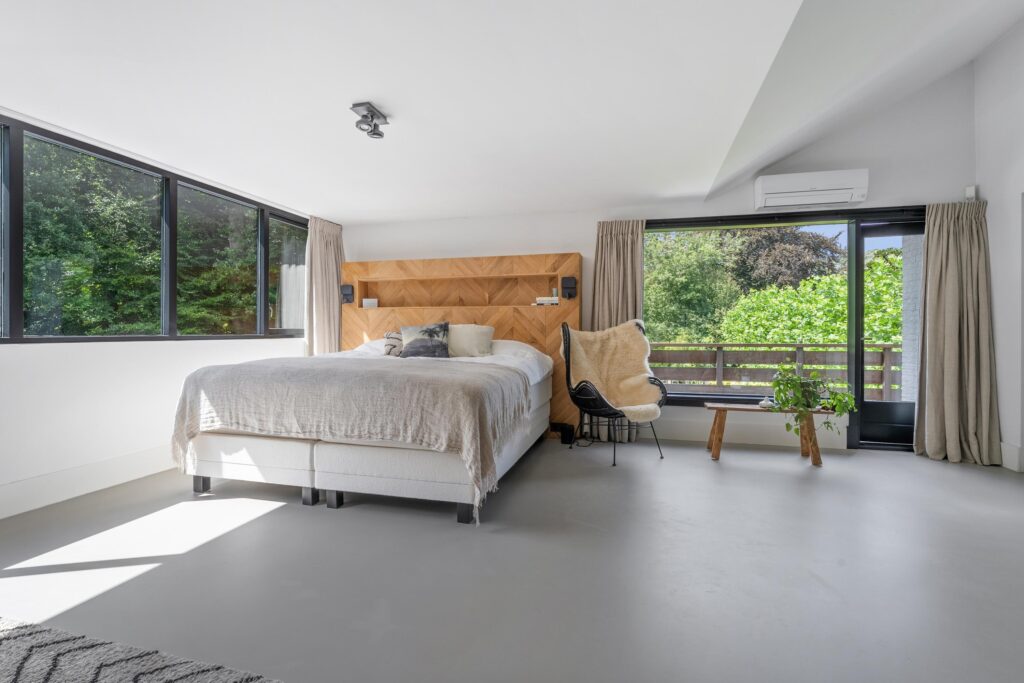 Spacious bedroom with large windows and wooden headboard.