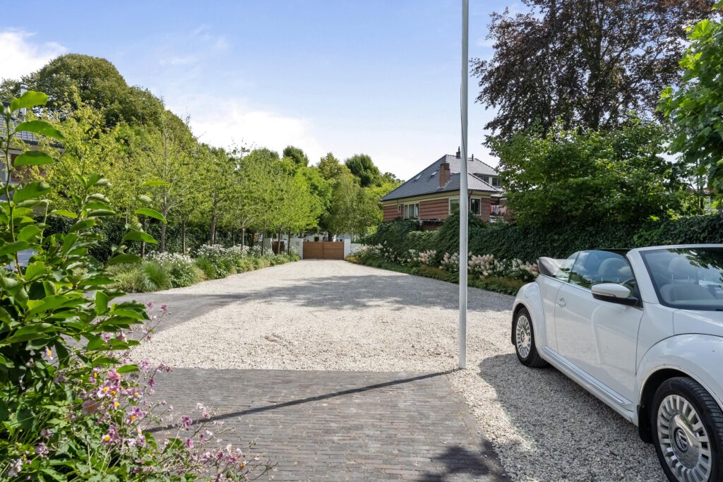 Gravel driveway with car, trees, and house.
