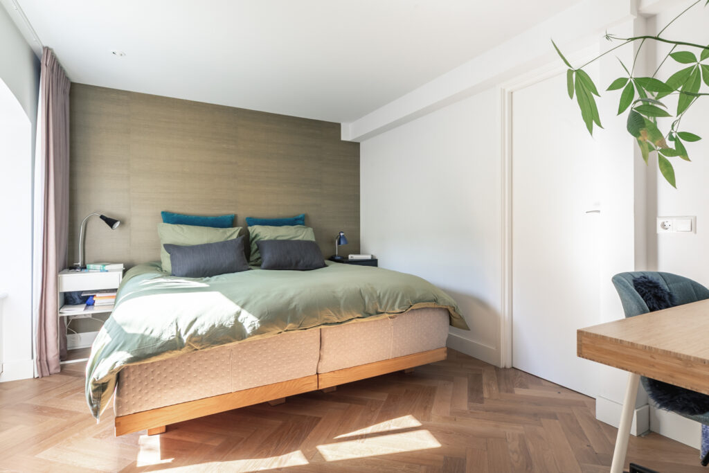Cozy bedroom with green bedding and wooden floor.