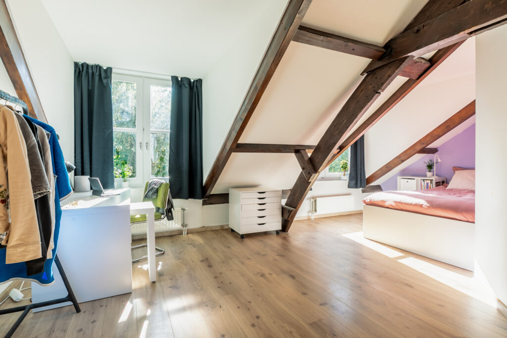 Cozy attic bedroom with wooden beams and desk.