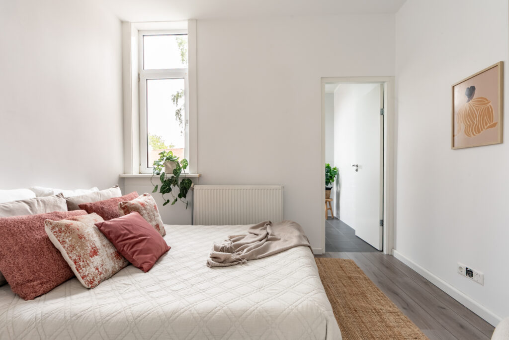 Minimalist bedroom with decorative pillows and window plant.