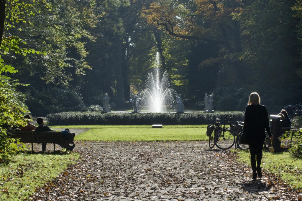 Person walking towards park fountain under trees