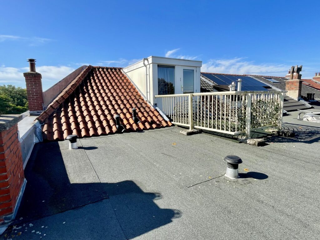 Rooftop with tiles and chimney under blue sky.