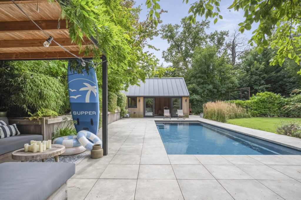 Backyard pool with modern cabana and lush greenery.