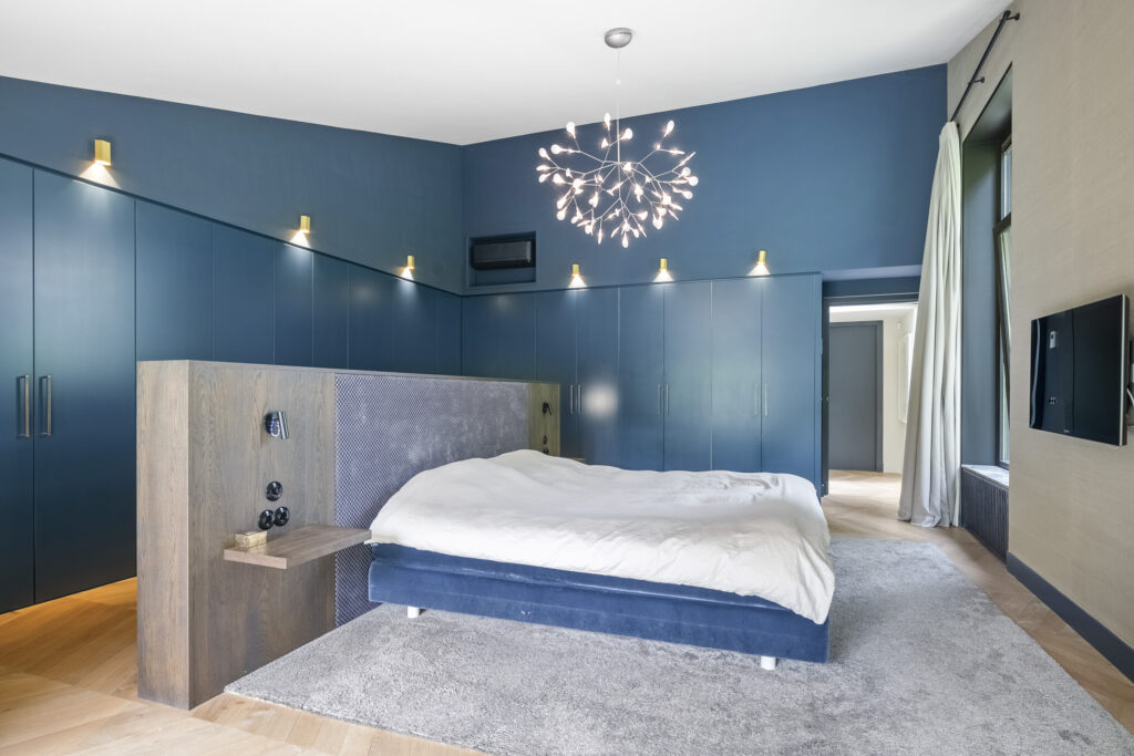 Elegant modern bedroom with blue decor and chandelier.