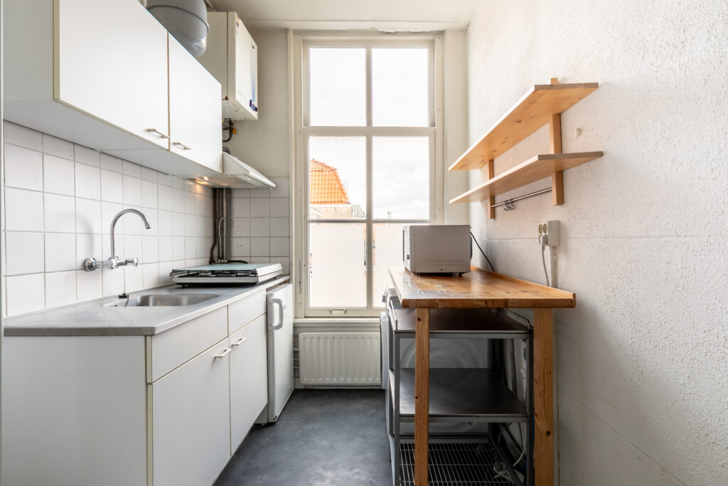 Compact kitchen with window, sink, and wooden shelves.