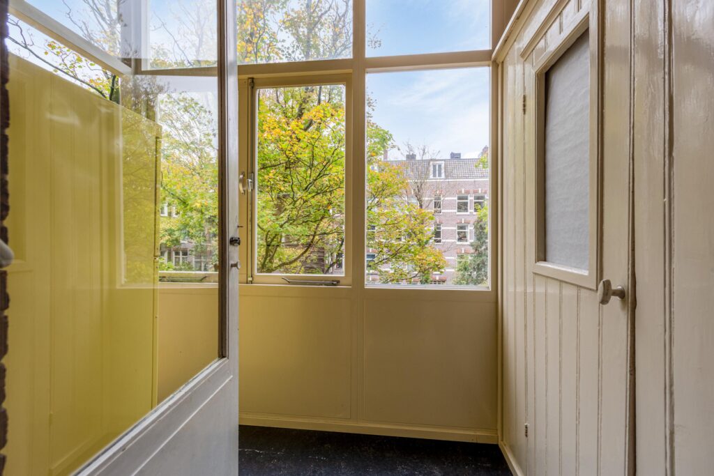 Open door to sunny balcony with trees outside.