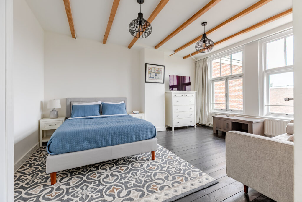 Modern bedroom with blue bedding and large windows.