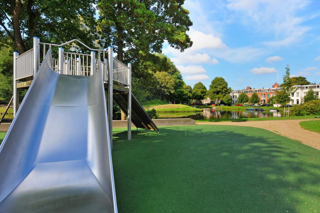 Playground slide in a park with trees and lake.