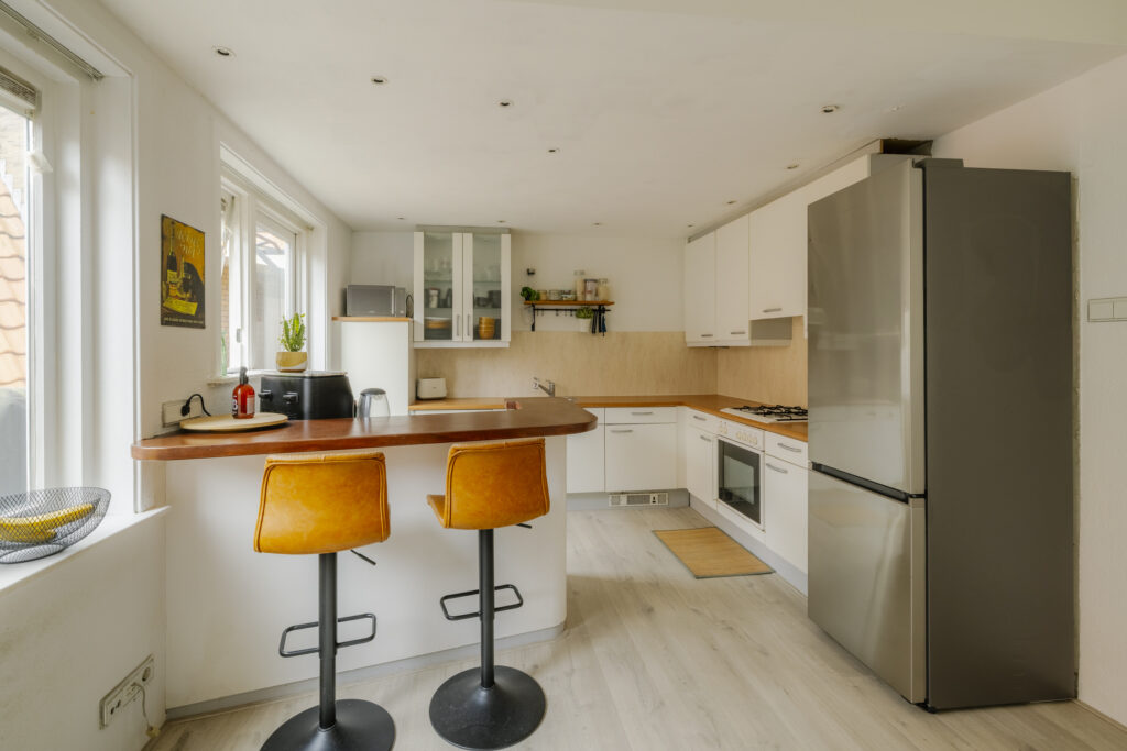 Modern kitchen with bar stools and stainless fridge.