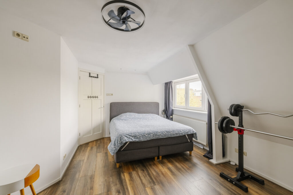Bedroom with bed, weights, and window view.