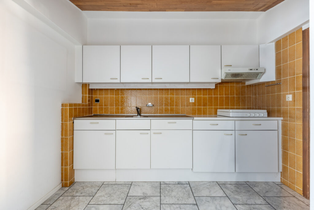 White kitchen with brown tiles and marble floor.