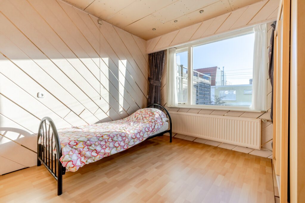 Sunny bedroom with single bed and large window.