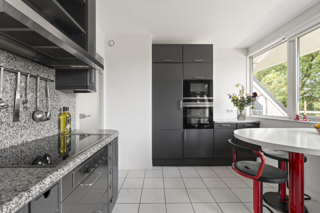 Modern kitchen with black cabinets and red chairs.