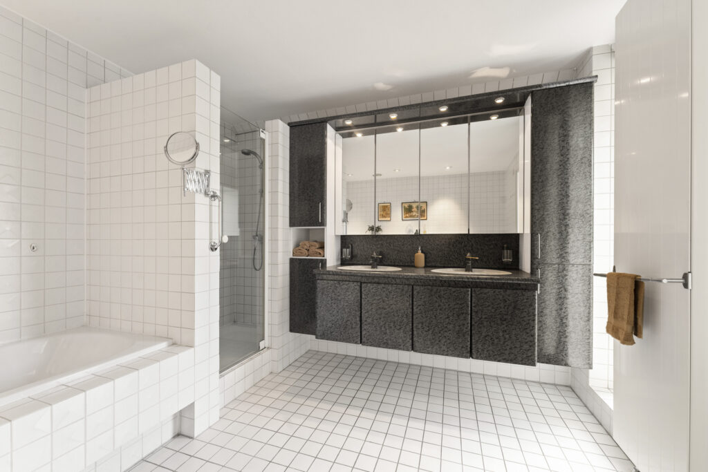 Modern bathroom with double sink and tiled shower.