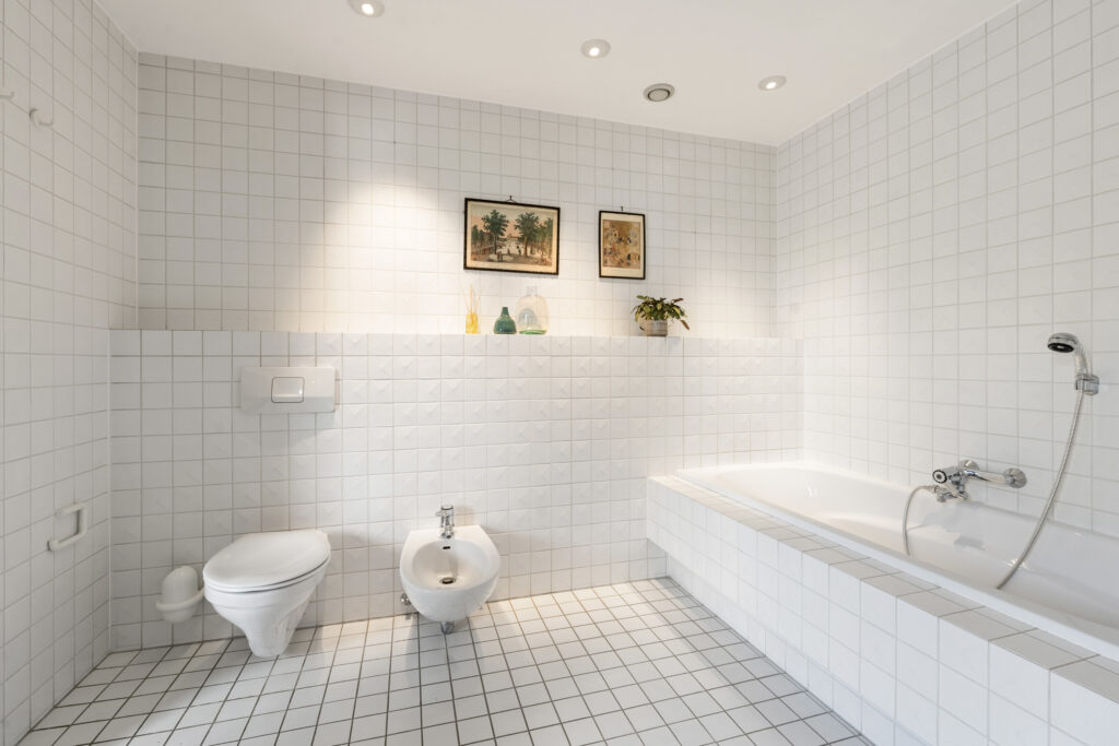 Modern white tiled bathroom with bathtub and toilet.