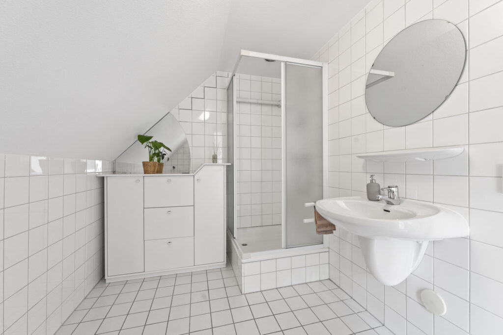 Modern white tiled bathroom with shower and sink.