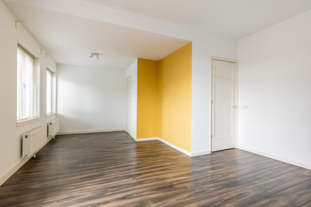 Empty room with wood floor and yellow accent wall.