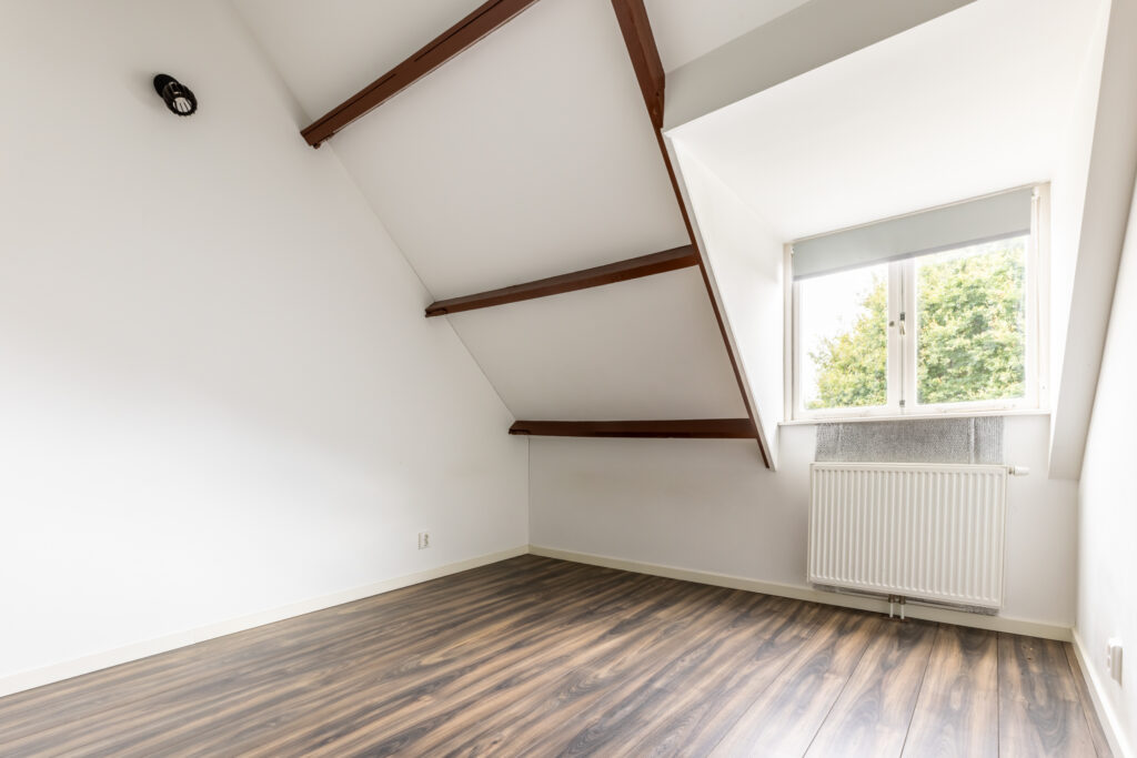Empty attic room with wooden floor and window.
