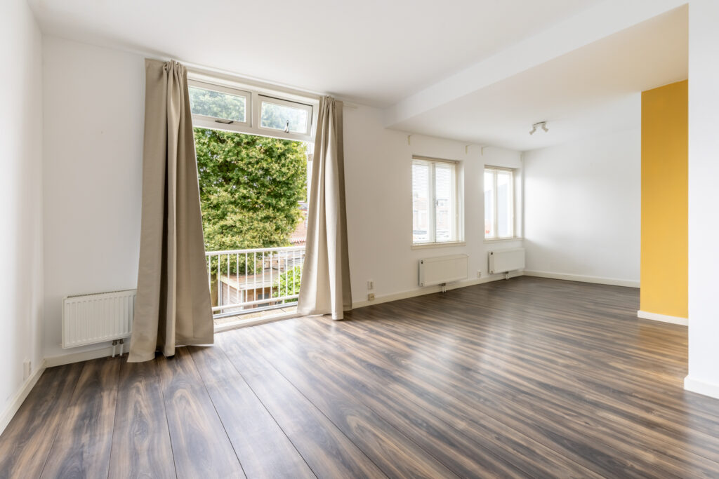 Bright empty room with large windows and wood flooring.