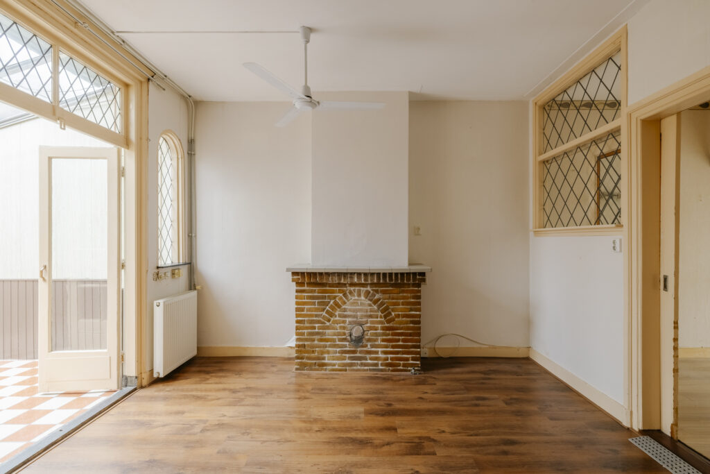 Empty room with brick fireplace and wooden floor.