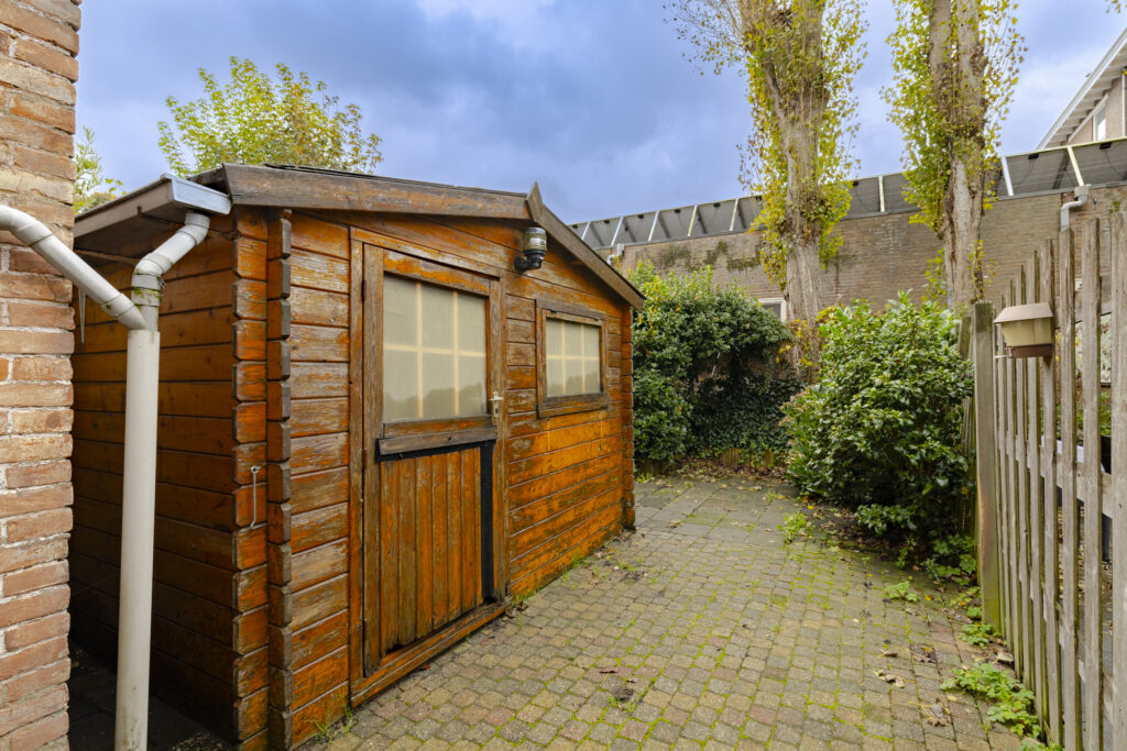 Wooden garden shed with brick path and greenery.