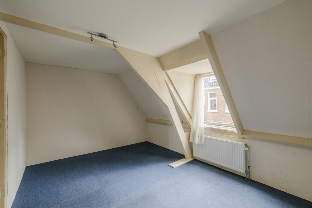 Empty attic room with blue carpet and window.
