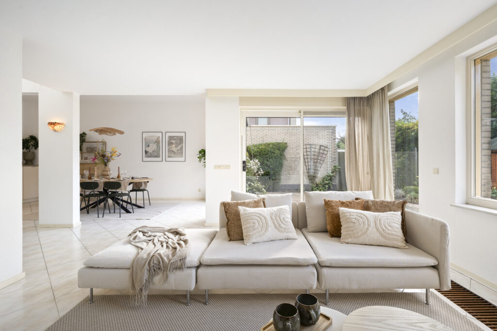 Modern living room with neutral decor and large windows.