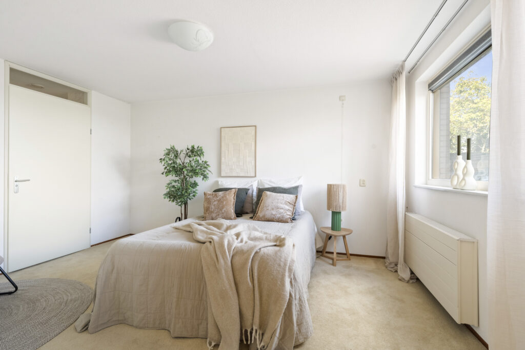 Cozy bedroom with bed, lamp, and window view.