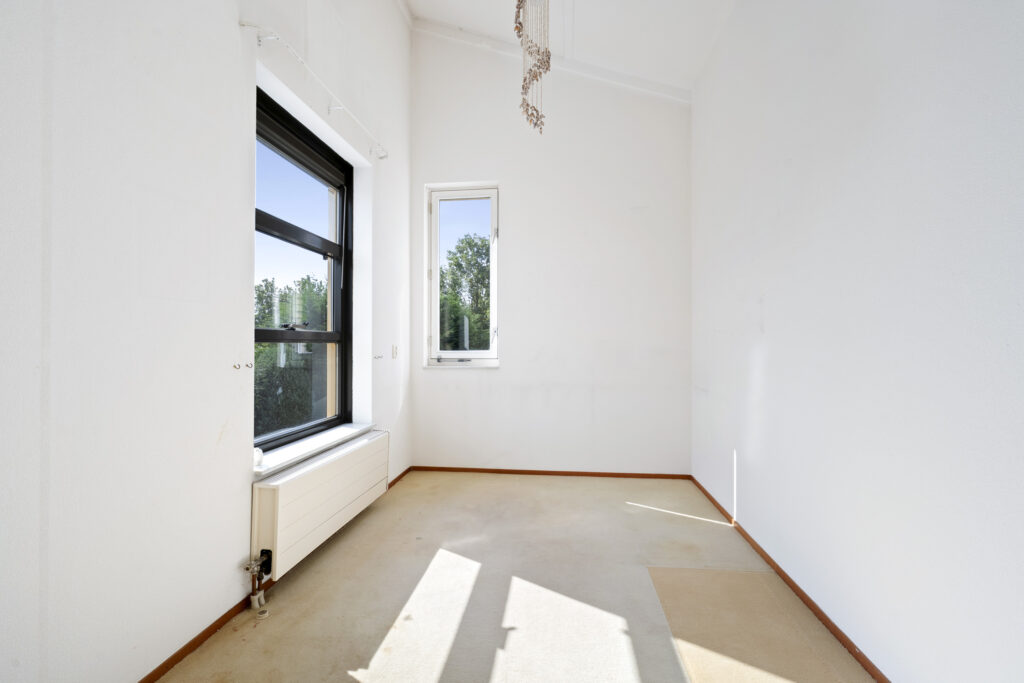 Bright empty room with windows, white walls, and radiator.