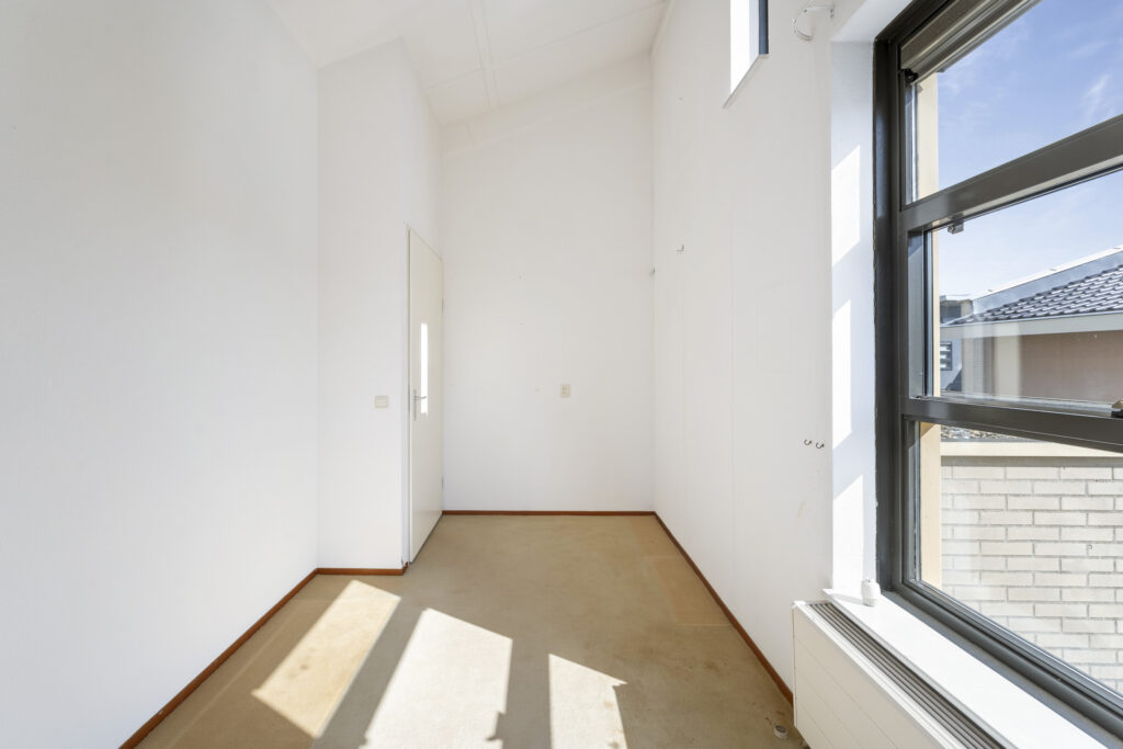Empty, sunlit room with beige carpet and window.