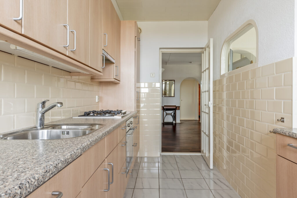 Modern kitchen with light wooden cabinets and white tiles.