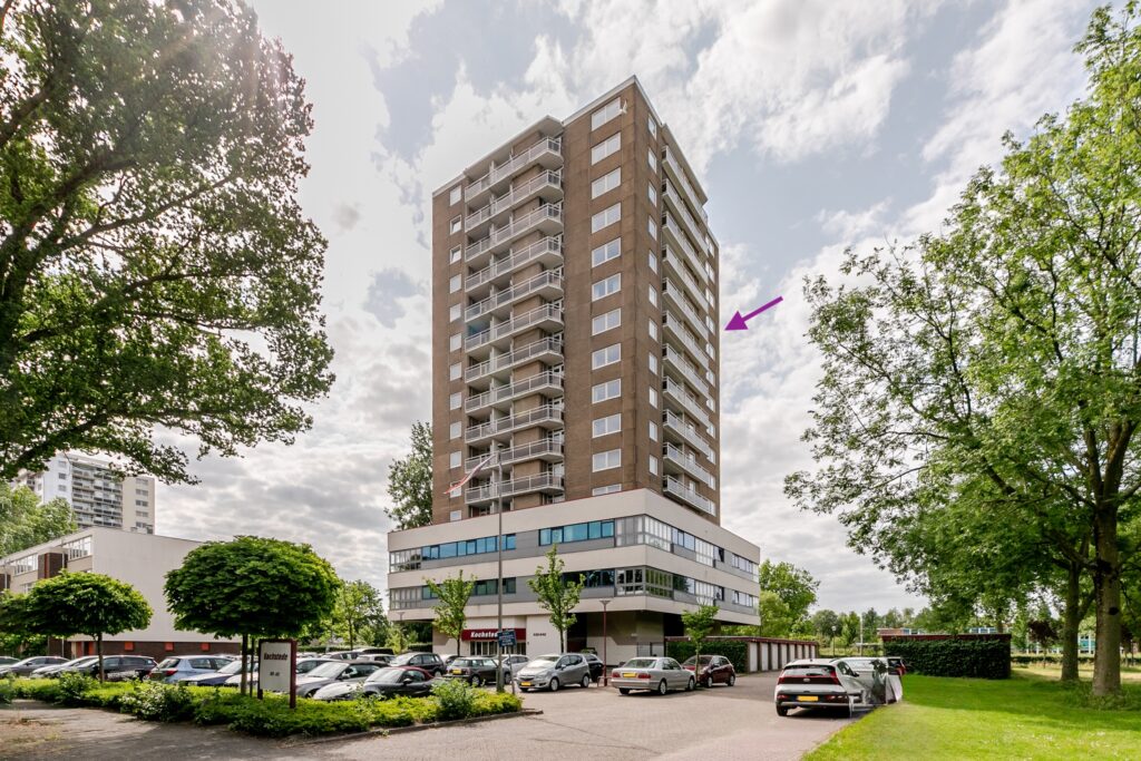 Tall apartment building with trees and parked cars.