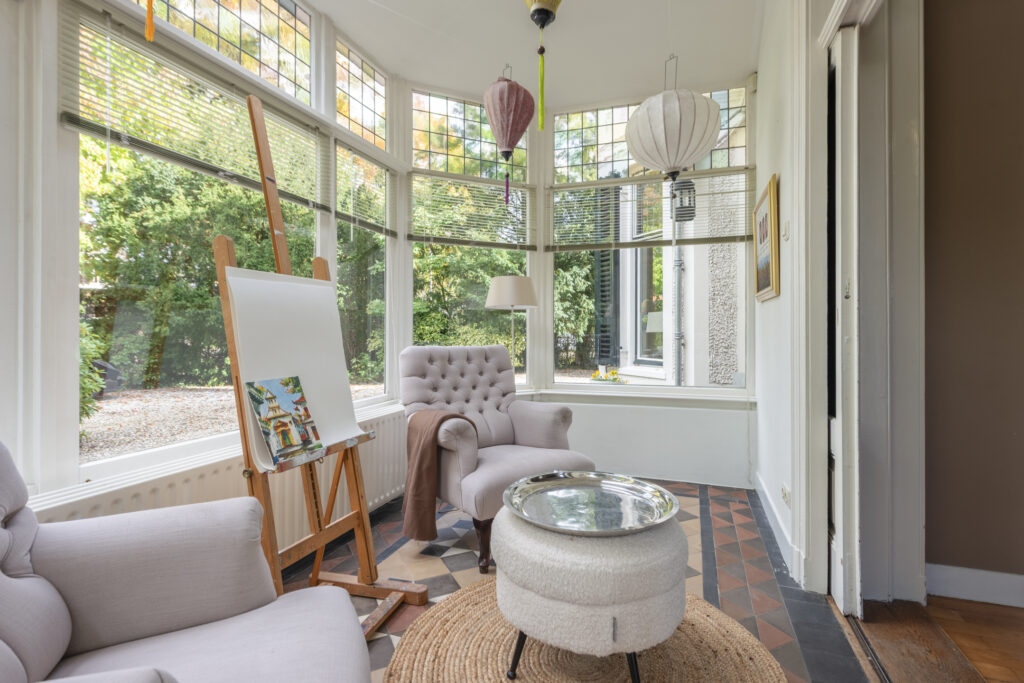 Cozy sunlit room with easel and armchairs.