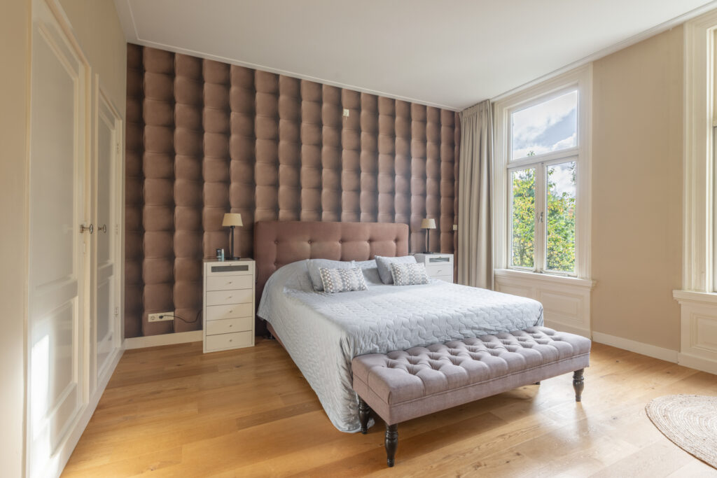 Cozy bedroom with tufted headboard and large windows.