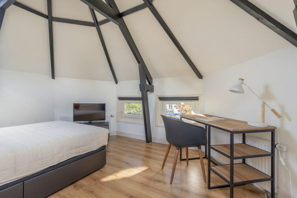 Cozy attic bedroom with desk and TV.