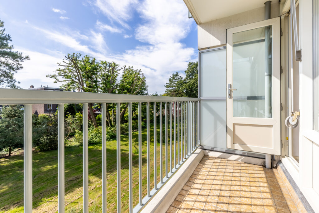 Sunny balcony overlooking green garden with trees.