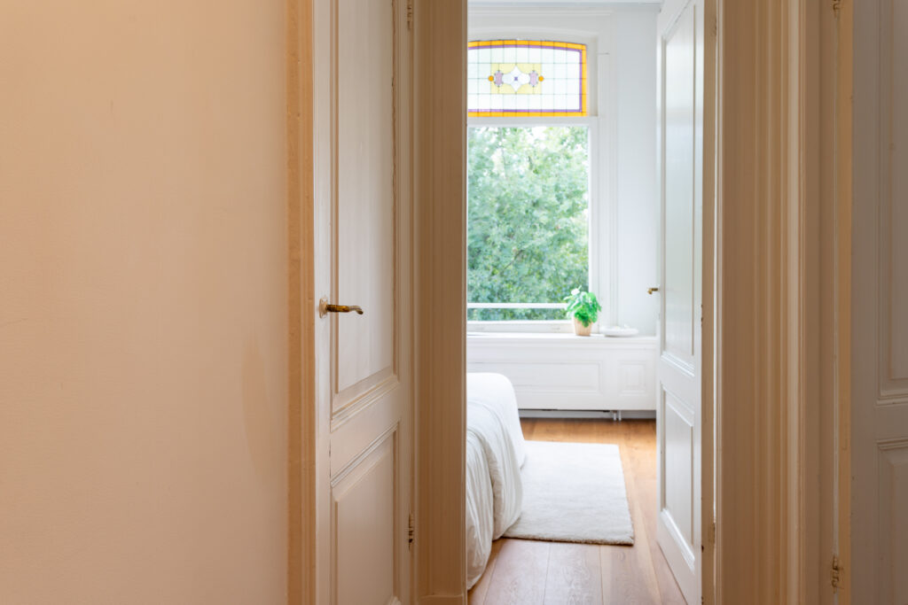 Bright bedroom through open door with stained glass window.