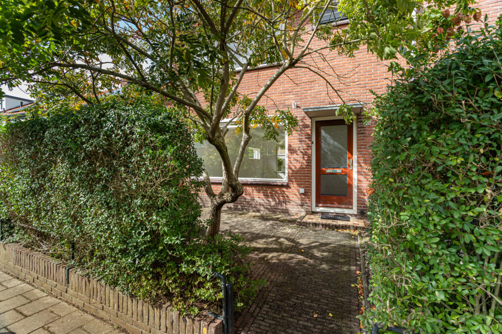 Brick house with tree and hedges outside.