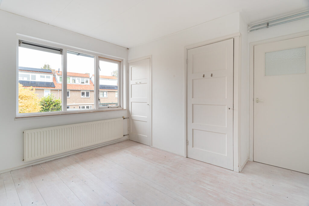 Empty white room with window and light wood floor.