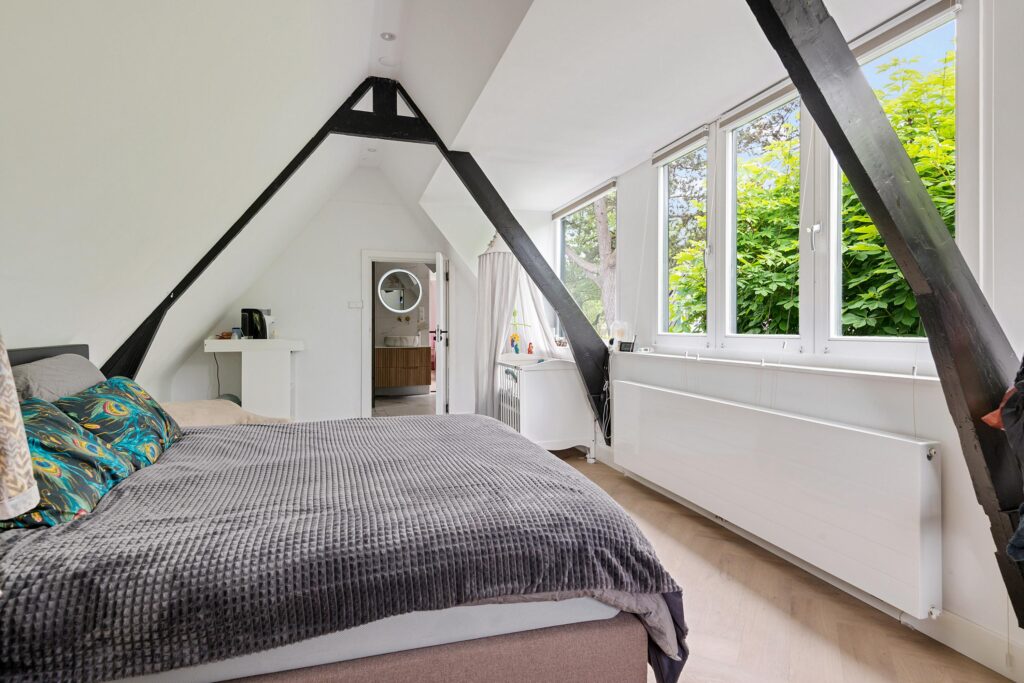 Cozy attic bedroom with large windows and beams.
