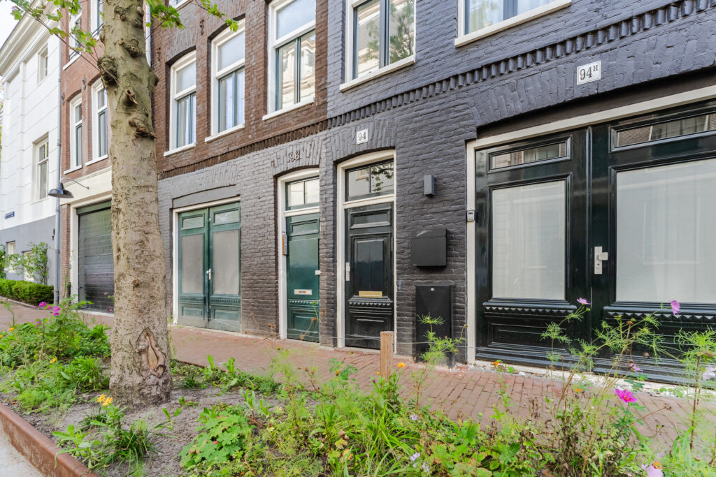 Brick townhouse exterior with green doors and plants.