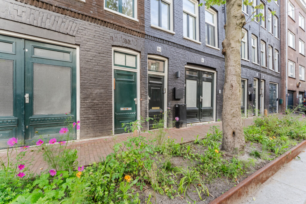 Brown brick building with green doors and flower garden.