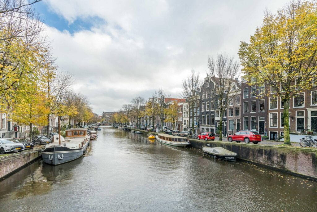 Canal in Amsterdam with boats and autumn trees.