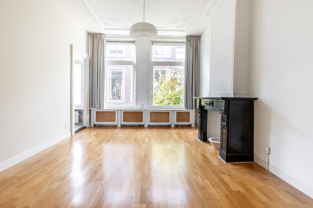 Bright empty room with wooden flooring and fireplace.