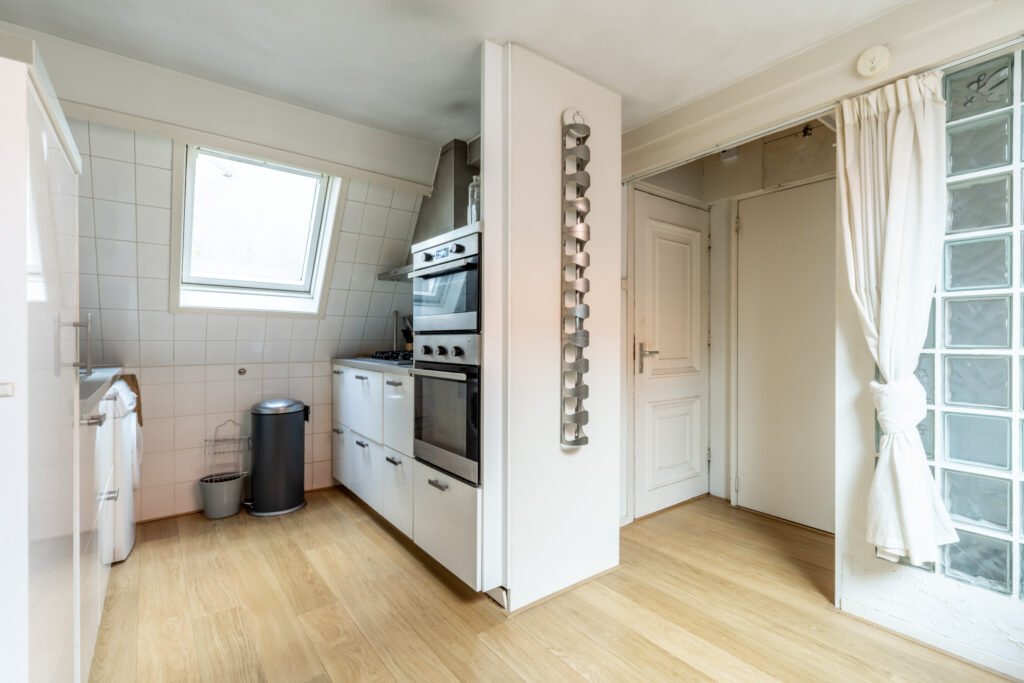 Modern white kitchen with wooden floor and appliances.