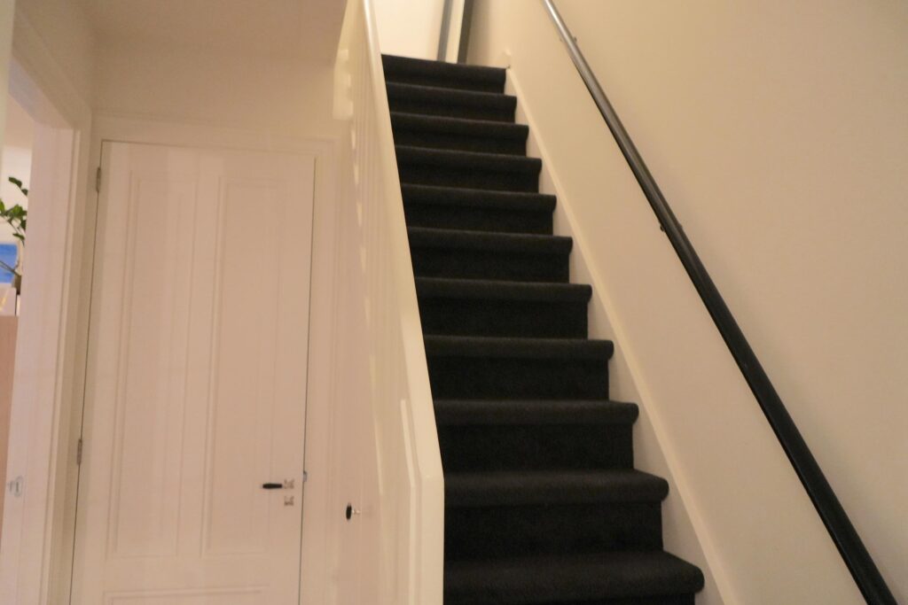 Indoor staircase with black carpet and railing.