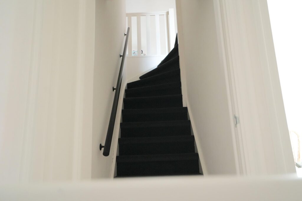 Narrow staircase with black carpet and handrail.