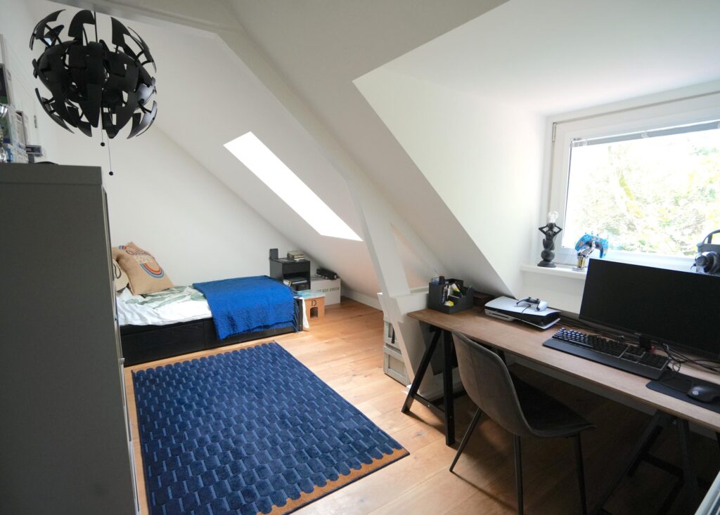 Cozy attic bedroom with desk and window view.