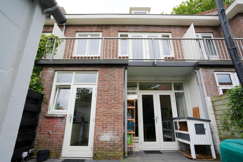 Two-story brick house with balcony and garden.